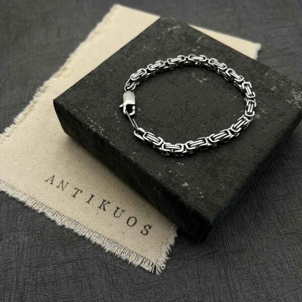 Silver chain bracelet on black textured background.