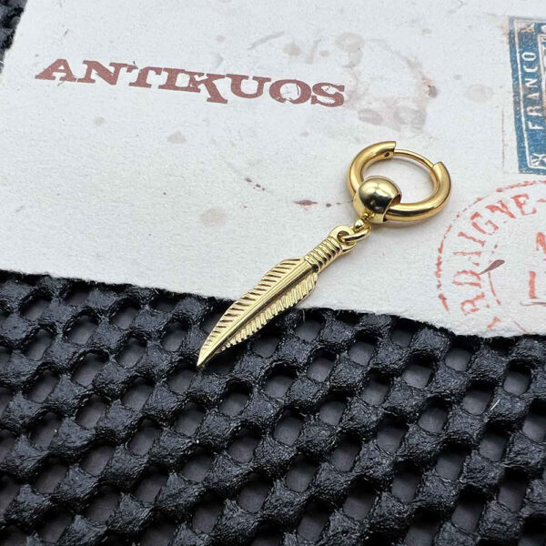 Gold hoop earring with feather charm on table.