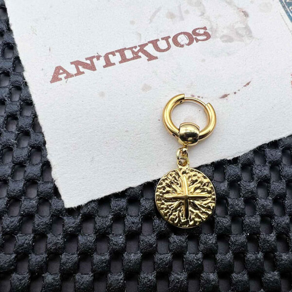 Gold earring with textured round pendant on paper.