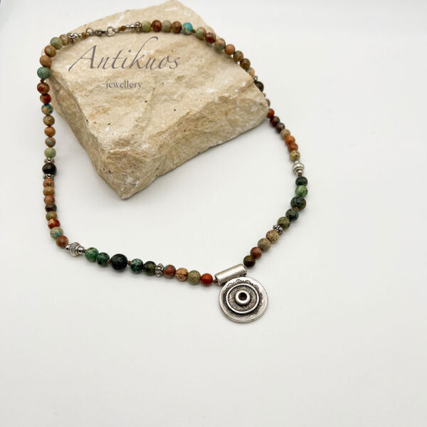 Colourful gemstone necklace with round pendant on stone.